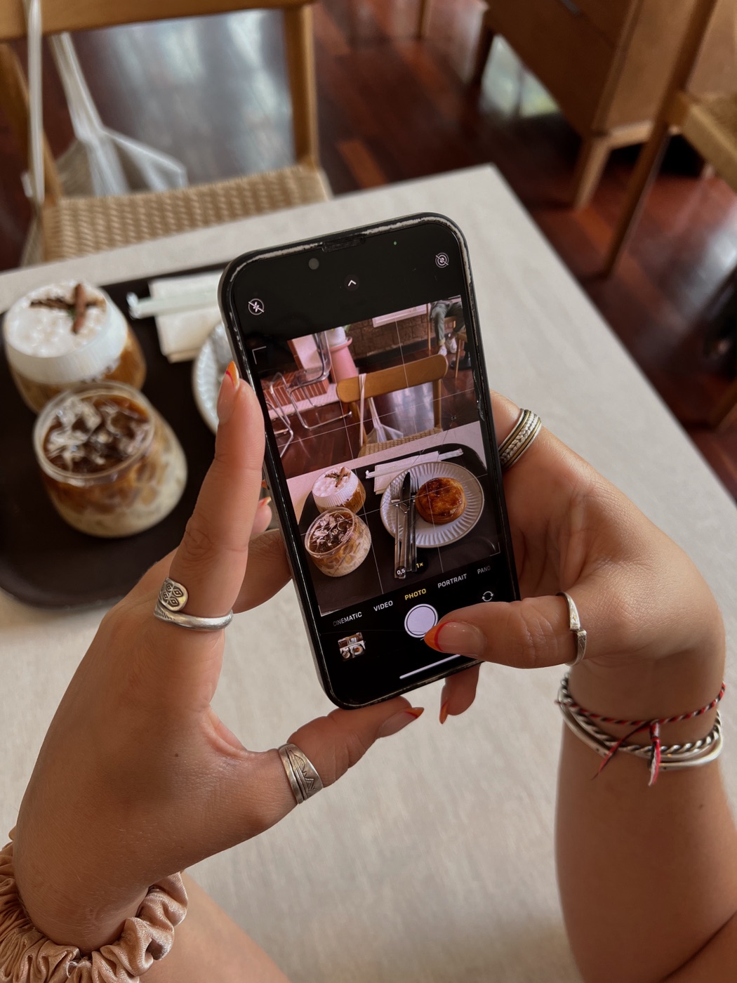 Mão segurando um celular fotografando cafés e uma sobremesa numa mesa, bastidores da produção de conteúdo para publi