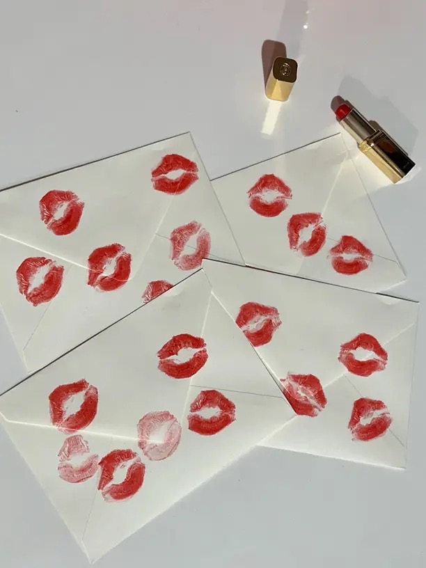 Batom vermelho e marcas de beijo em envelopes brancos