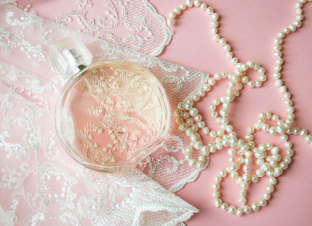 Frasco de perfume sobre renda rosa com colar de pérolas
